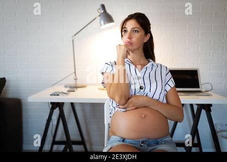 Stanco donna incinta che lavorano da casa su computer Foto Stock