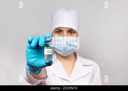 Un medico o un tecnico di laboratorio detiene un vaccino contro il morbillo. Epidemia di morbillo, encefalite da morbillo. Il concetto di vaccinazione nell'assistenza sanitaria Foto Stock