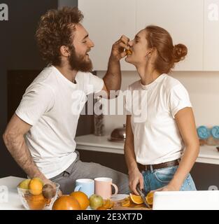 Il ragazzo si nutre o allatta la sua ragazza. Bella giovane coppia che si nutrono a vicenda facendo divertimento in cucina moderna e sorridendo mentre cucinare a casa Foto Stock