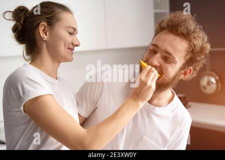 Bella ragazza si nutre o allattando il suo ragazzo. Bella giovane coppia che si nutrono a vicenda facendo divertimento in cucina moderna e sorridendo mentre cucinare a casa. Foto Stock