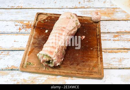 Preparazione di una porchetta con una miscela di erbe aromatiche posto su un pezzo di pancia di maiale fresco aperto in lo spessore Foto Stock