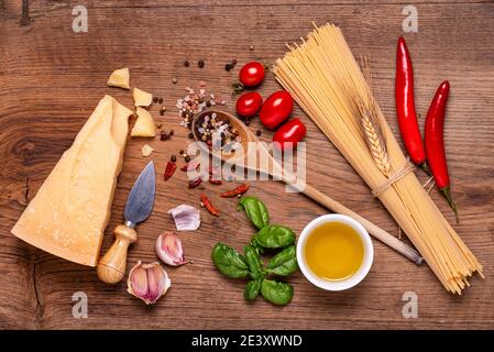 Tavola, spaghetti crudi, formaggio Grana Padano stagionato, aglio, olio e numerosi ingredienti con erbe aromatiche. Vista dall'alto Foto Stock