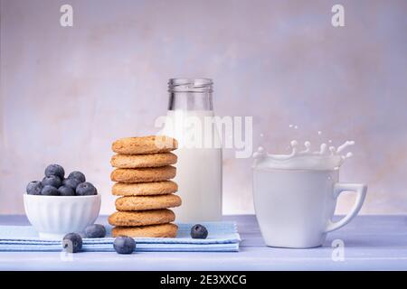 sul tavolo blu lavanda, la colazione con biscotti integrali con shortbread, mirtilli e latte fresco con spruzzi Foto Stock