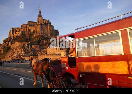 Le Mont Saint-Michel in inverno. Ora d'oro. Sulla diga in fondo al monte, arrivo di la Maringote', una navetta trainata da cavalli trainata da due dra Foto Stock