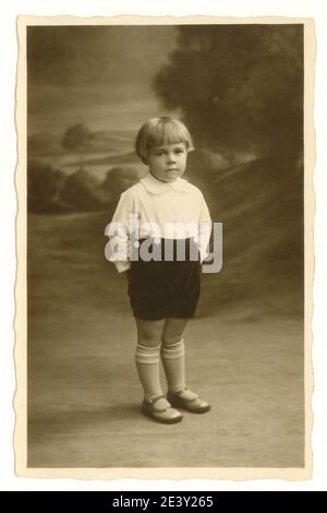 Originale primo 1900's studio ritratto foto di ragazzo di circa 3 anni con pettinatura bob, in piedi aspetto serio, Regno Unito circa 1925 Foto Stock