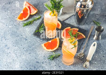 Due bicchieri di cocktail Paloma con succo di pompelmo fresco di tequila e rosmarino. Superficie in cemento grigio. Foto Stock