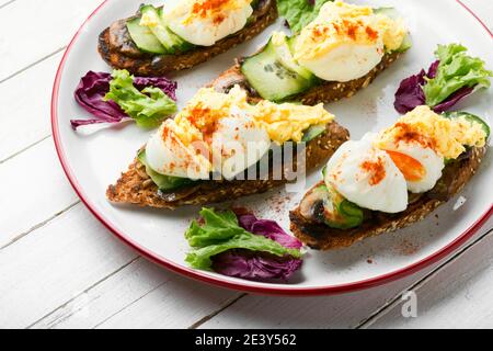 Bruschetta con uova in camicia, cetriolo e funghi. Gustose uova Benedetto sul piatto Foto Stock