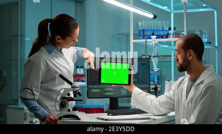 Moderno laboratorio di ricerca medica con due scienziati che utilizzano tablet con schermo verde cromatico, parlando. Medici specialisti discutere di trattamento innovativo, laboratorio scientifico avanzato per la medicina. Foto Stock