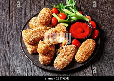 Suppli al telefono fast food italiano - crocchette di riso fritto farcite con mozzarella servite su un piatto nero con gambi di sedano, pomodori e ketchup Foto Stock