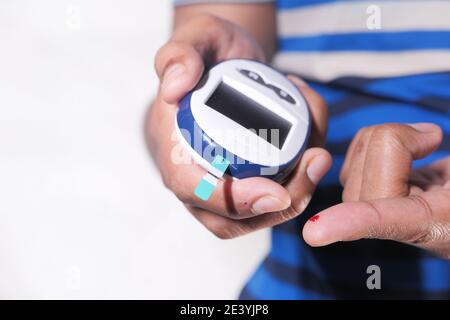 primo piano della mano dell'uomo diabetico controllare il livello di zucchero nel sangue bianco isolato Foto Stock