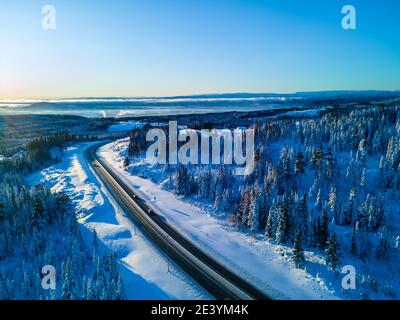 Autostrada con auto che attraversa un passo di montagna con alberi innevati. Foto Stock