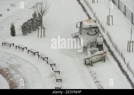 il trattore-escavatore rimuove la neve nel cortile della città. lavoro di servizi pubblici Foto Stock