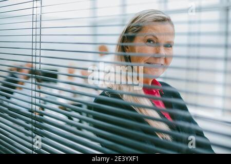 donna di affari riuscita che guarda attraverso le persiane della finestra. Foto Stock