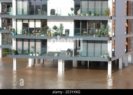 Hereford, Herefordshire - Giovedi 21 gennaio 2021 - UN uomo si siede sul balcone del suo blocco di appartamenti lungo il fiume, mentre il fiume Wye si inonda sotto i suoi palafitte rialzati - il Wye dovrebbe picco questa sera a 5.3 metri. Photo Steven May / Alamy Live News Foto Stock