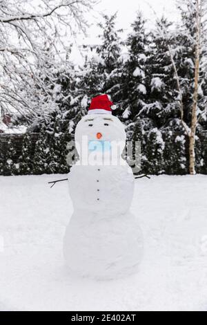 Pupazzo di neve in una maschera medica protettiva. Foto concettuale dell'impatto del virus covid-19 sulla vita quotidiana. Foto Stock