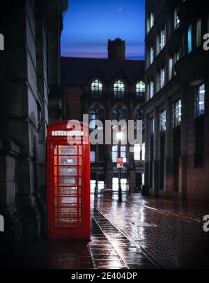 Strada deserta di notte con il tradizionale telefono reale rosso britannico box illuminato luce che riflette sull'acqua dopo la pioggia chiaro notte cielo luna inquietante vista Foto Stock