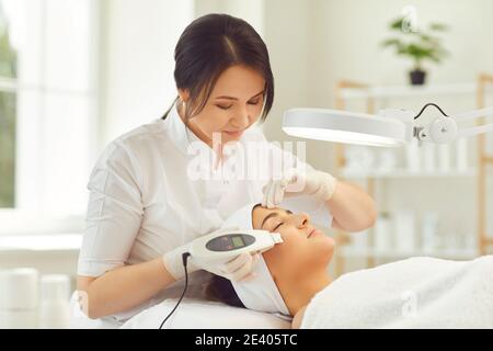 Dermatologist sorridente che fa gli apparecchi di ecografia pulizia facciale per la donna giovane Foto Stock