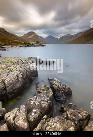 Rocce frastagliate sulla costa di Wastwater con spettacolari nuvole e montagne sullo sfondo. Lake District National Park, Regno Unito. Foto Stock