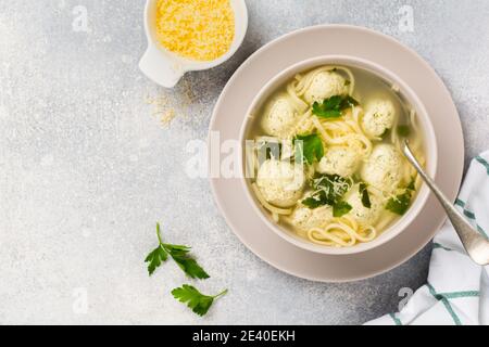 Ciotola di zuppa italiana tradizionale con polpette di pollo e pasta d'uovo, parmigiano, prezzemolo su sfondo grigio. Cucina italiana tradizionale. Foto Stock