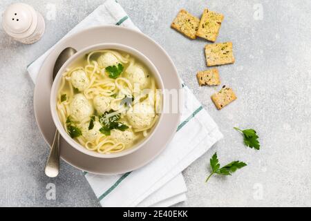 Ciotola di zuppa italiana tradizionale con polpette di pollo e pasta d'uovo, parmigiano, prezzemolo su sfondo grigio. Cucina italiana tradizionale. Foto Stock