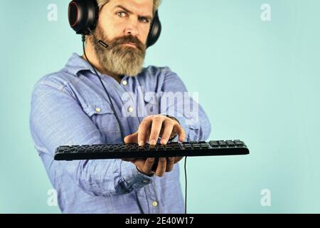 Cyber arena sportiva. Guida alla creazione di PC per il gaming. Impostazioni grafiche. Dipendenza da gioco. Cuffie e tastiera per giocatori hipster con cuscinetti da uomo. Giocare ai giochi per computer. Piattaforma di gioco online. Gioco moderno tempo libero. Foto Stock