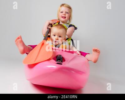 Due bambini in kayak rosa con pagaia arancione Foto Stock