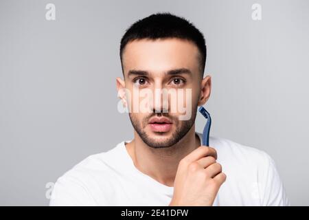giovane uomo ispanico che guarda la fotocamera mentre si rade isolato grigio Foto Stock