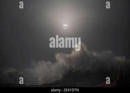 Pericoloso grande onda di mare splash in una notte di luna piena overcast. Foto Stock