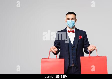 elegante uomo ispanico in maschera medica con borse rosse isolato su grigio Foto Stock