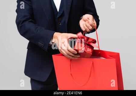 vista ritagliata di uomo che mette scatola regalo in rosso shopping sacchetto isolato in grigio Foto Stock