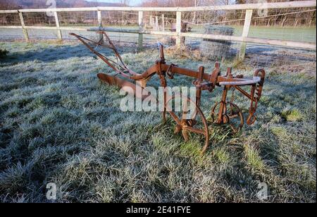 Un vecchio aratro rustico in ferro riposa in un campo gelido Nel mese di gennaio inverno sole geloso campo in Sussex est Foto Stock