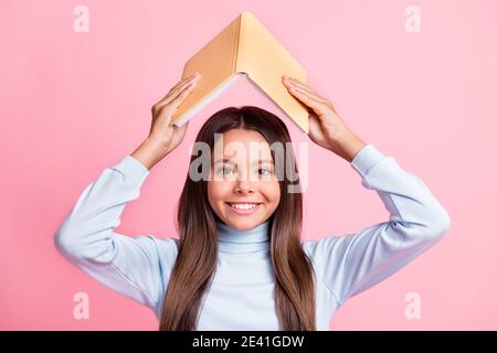 Primo piano ritratto di bella ragazza allegra che tiene il libro sopra la testa conoscenza isolata su sfondo di colore pastello rosa Foto Stock