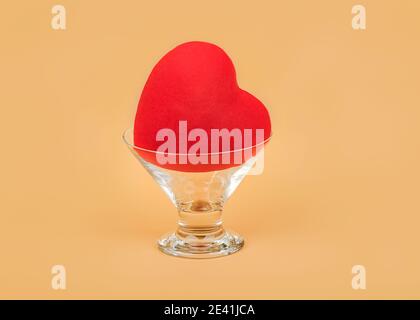 Cuore rosso all'interno di una tazza di vetro su sfondo beige.giorno di San Valentino concetto Foto Stock