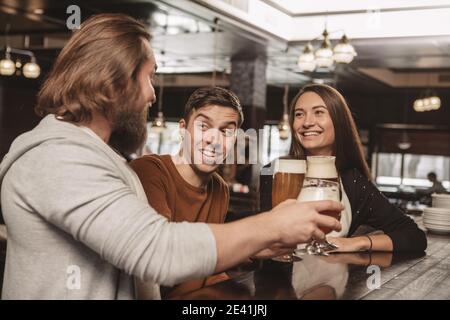 Bel giovane sorridente felice, godendosi il riposo al bar con i suoi amici. Gruppo di amici che beve al pub della birra locale. Due uomini e essere Foto Stock