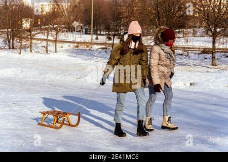 POZNAN, POLONIA - 17 gennaio 2021: Due ragazze che tirano una slitta di legno sulla neve in un parco in una fredda giornata invernale. Foto Stock