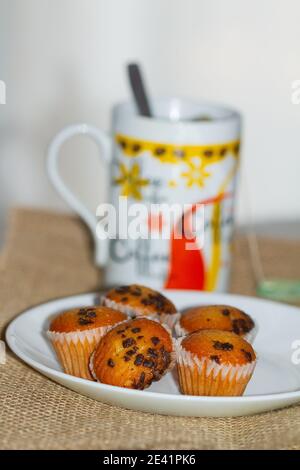 Una piccola tazza di muffin al cioccolato su un piatto bianco con sfondo della tazza di caffè sfocato Foto Stock