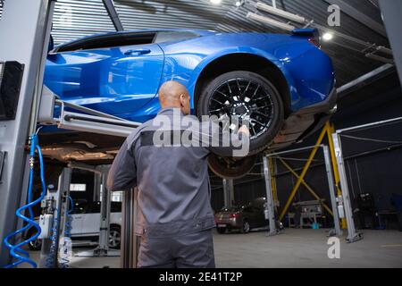 Vista posteriore a basso angolo di un addetto alla manutenzione di un'automobile che esamina l'automobile sollevata, spazio di copia Foto Stock