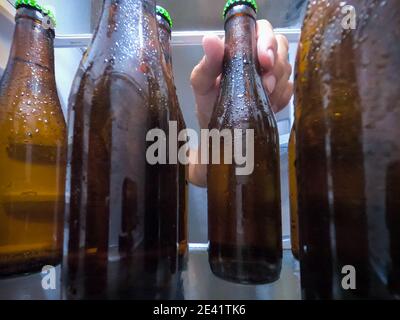 Una mano che preleva una bottiglia di birra ghiacciata dal frigorifero. Concetto di birra Foto Stock