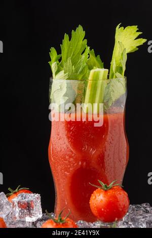 Primo piano di vetro di cristallo con cocktail e sedano sanguinoso mary, con gelato e pomodori ciliegini, su fondo nero, verticale Foto Stock