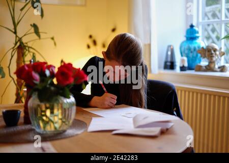 Una giovane ragazza si siede a un tavolo in un soggiorno che studia ad Addingham, West Yorkshire. REGNO UNITO. Foto Stock