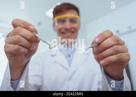 Esame medico, concetto di cura dentale. Fuoco selettivo sugli attrezzi dentali nelle mani del dentista allegro. Buon dentista professionista che raggiunge Foto Stock