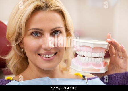 Primo piano di una splendida donna matura che sorride gioiosamente tenendo muffa dentaria, in posa presso la clinica dentale. Attraente paziente di sesso femminile in visita dentista. Denti, Foto Stock