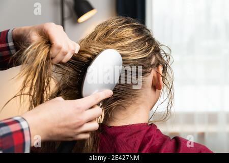 Il parrucchiere pettina i capelli con un pennello per una donna bionda che si prepara per la procedura dei capelli. A casa o in salone. Foto Stock