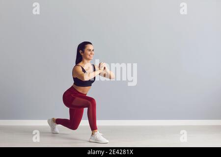 Una giovane donna sorridente in forma che fa affondo in avanti durante uno sport allenati in palestra Foto Stock