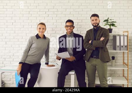 Team di tre giovani uomini d'affari felici e fiduciosi che guardano fotocamera e sorridente Foto Stock