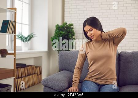 Donna strofinando il collo, sentendo dolore da osteocondrosi, nervo pizzicato o colpo di frusta Foto Stock