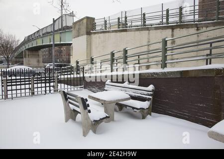 Tavolo coperto di neve e panchine in un parco tascabile situato accanto a un ponte pedonale nel quartiere Windsor Terrace di Brooklyn, New York. Foto Stock