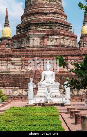 Mattoni rossi Wat Yai Chai Mongkhon antico tempio con verde cespugli parco e bianco seduto buddha a Bangkok, Thailandia durante il sole e calda giornata Foto Stock