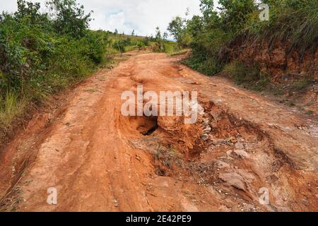 Polvere rossa e fango su strada in cattive condizioni con grandi buchi e protuberanze che si formano dopo la pioggia. I percorsi per il parco nazionale di Andringitra sono estremamente cattivi durante il bagnato Foto Stock