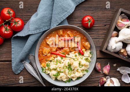 Stufato di maiale caldo con peperoncino, servito con gnocchi lessati con cipollotti su rustico fondo di legno Foto Stock